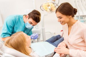 Pediatric dentist examining young patient with her mother in dental clinic